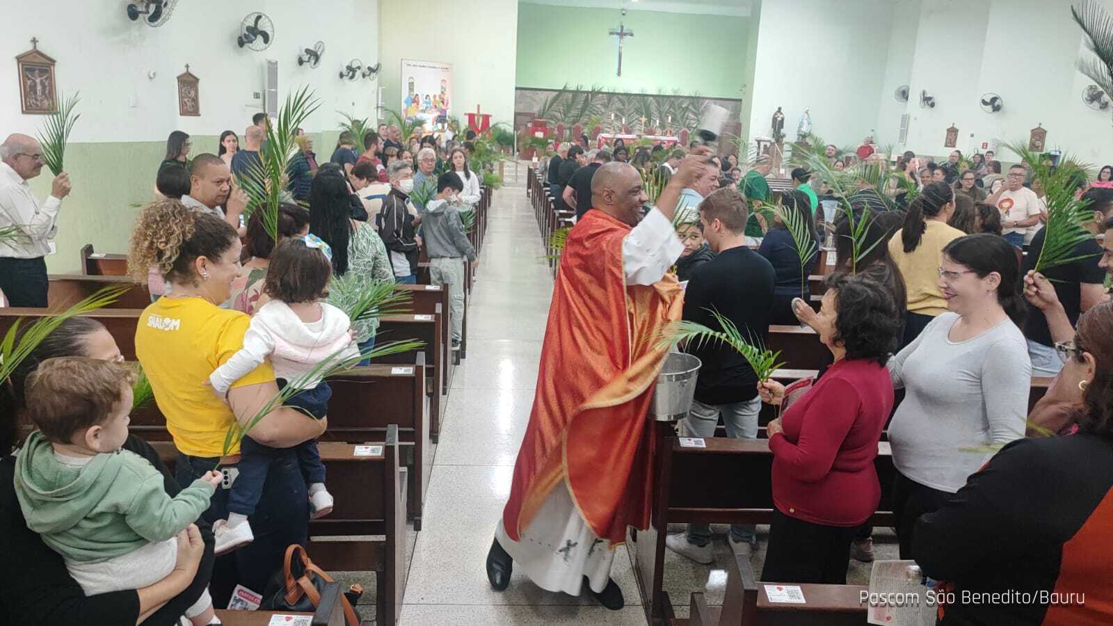 Padre aspergindo os ramos dos fiéis durante a celebração